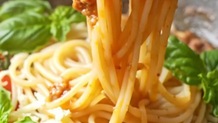 Twirled spaghetti coated in rich tomato meat sauce with melted mozzarella and fresh basil