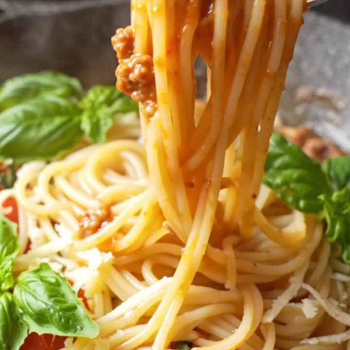 Twirled spaghetti coated in rich tomato meat sauce with melted mozzarella and fresh basil