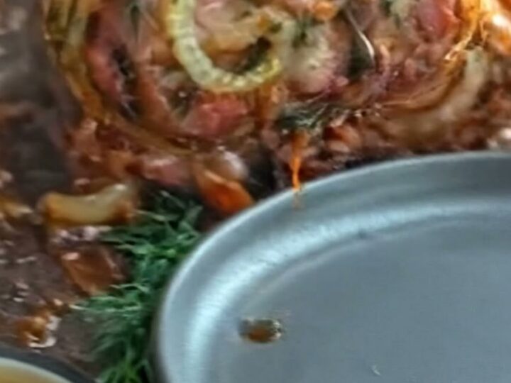 A sliced pork roulade showing a beautiful herb-filled spiral and crispy bacon crust.