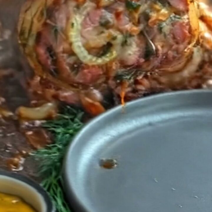 A sliced pork roulade showing a beautiful herb-filled spiral and crispy bacon crust.