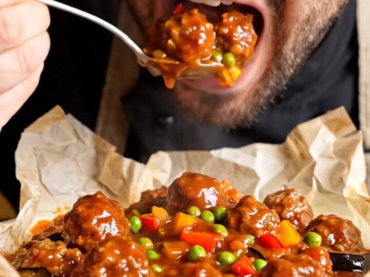 A baking dish filled with tender meatballs, golden eggplant and potatoes, peas, and peppers in a rich tomato sauce.