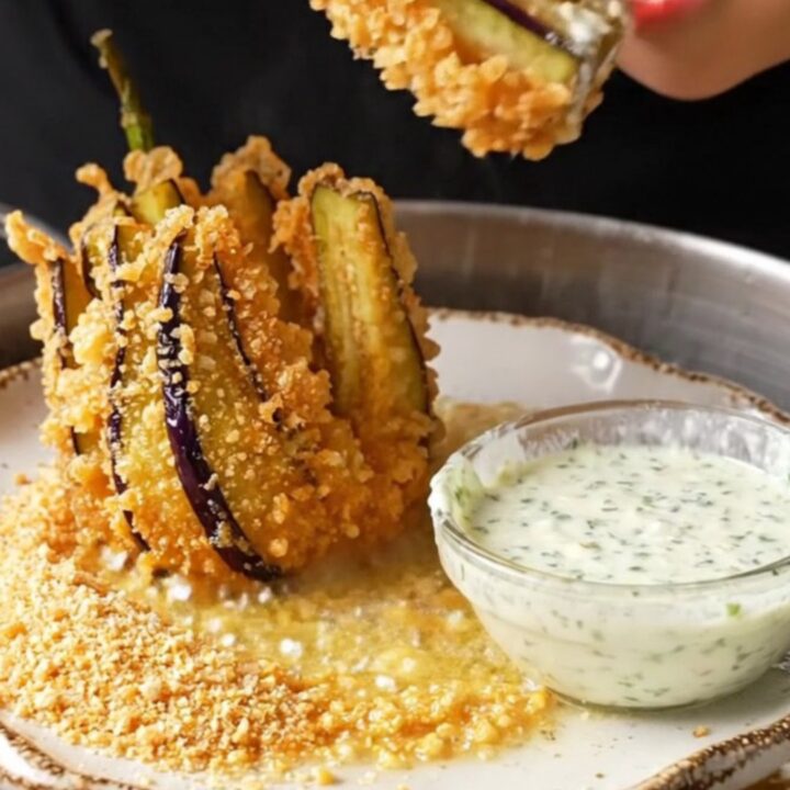 A golden fried eggplant fan on a white plate with a bowl of garlic herb yogurt dip