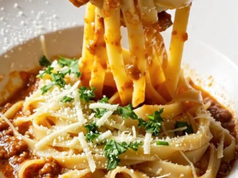 Twirled tagliatelle Bolognese in a skillet with melted mozzarella and Parmesan