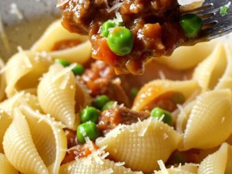 A bowl of shell pasta with beef and peas in a glossy tomato sauce, topped with grated Parmesan.