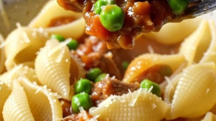A bowl of shell pasta with beef and peas in a glossy tomato sauce, topped with grated Parmesan.