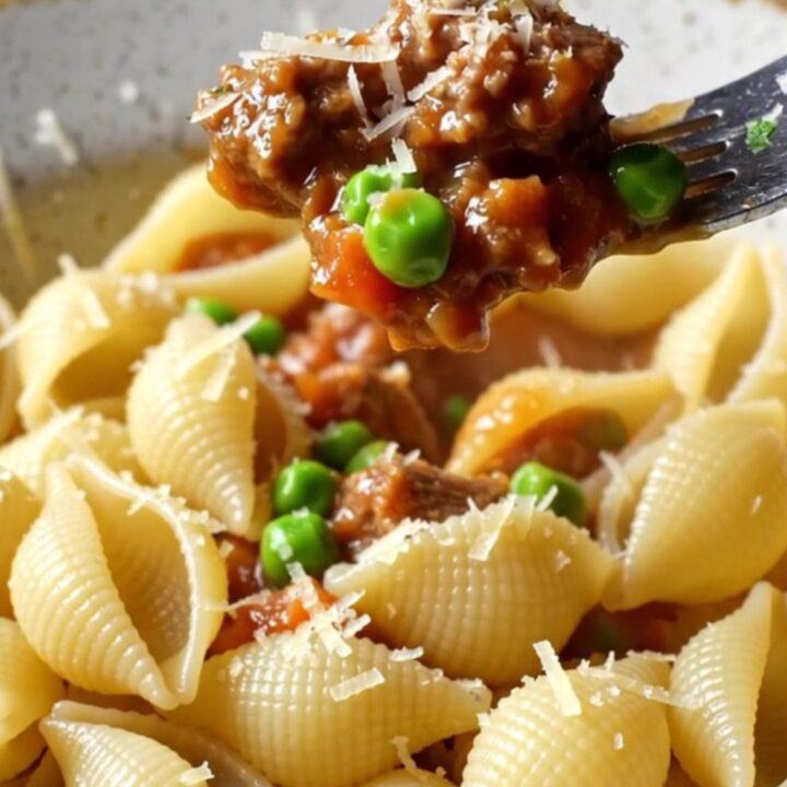 A bowl of shell pasta with beef and peas in a glossy tomato sauce, topped with grated Parmesan.