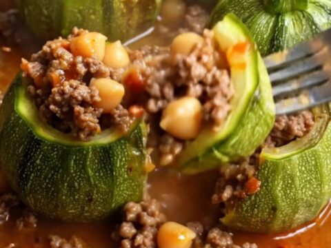 Braised stuffed round zucchini on a plate with tomato broth spooned over