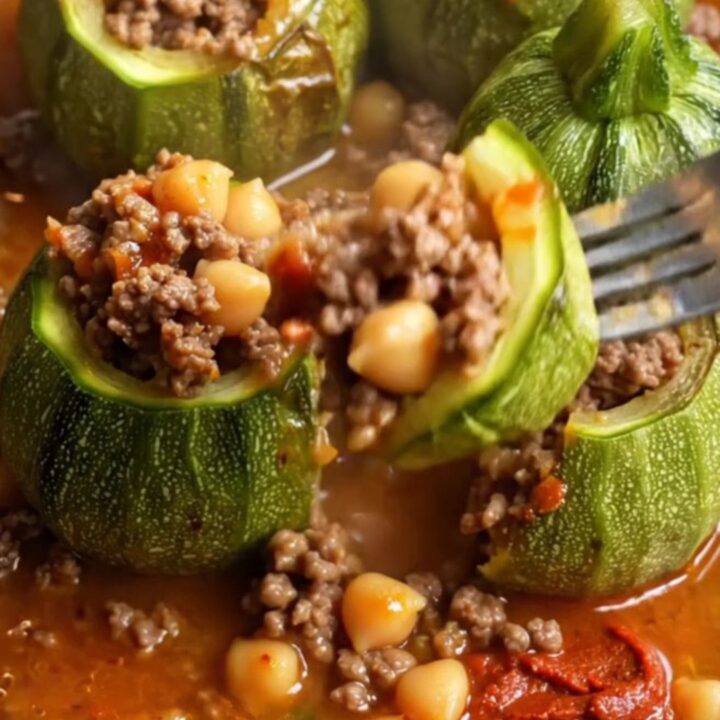 Braised stuffed round zucchini on a plate with tomato broth spooned over