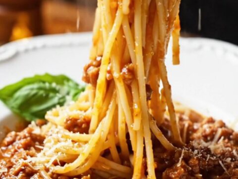 A towering forkful of spaghetti Bolognese twirled in a bowl, garnished with Parmesan and basil.