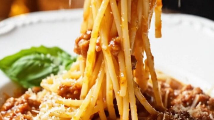 A towering forkful of spaghetti Bolognese twirled in a bowl, garnished with Parmesan and basil.