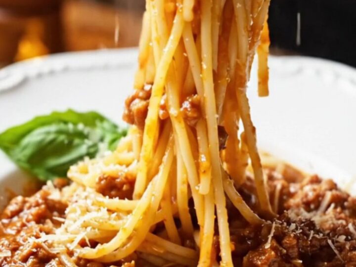 A towering forkful of spaghetti Bolognese twirled in a bowl, garnished with Parmesan and basil.