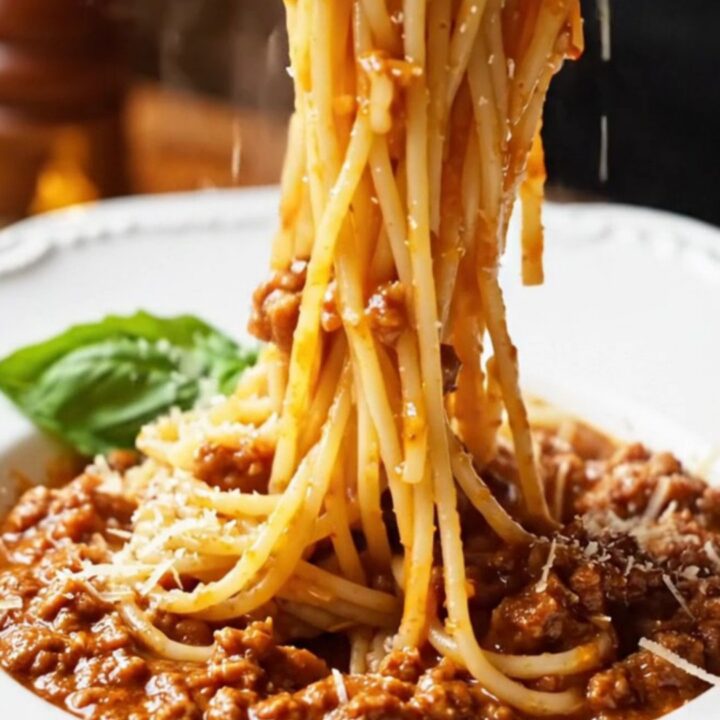 A towering forkful of spaghetti Bolognese twirled in a bowl, garnished with Parmesan and basil.