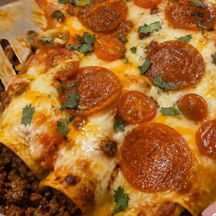 A spatula lifting a cheesy pepperoni enchilada from an oval baking dish, displaying a long elastic cheese pull.