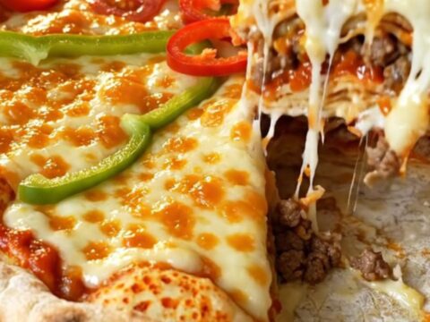 A tall layered lavaş pizza pie with golden melted cheese, cherry tomatoes, and green pepper on top