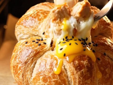 Golden bread pot pie with braided lid lifted, revealing molten cheese and chicken filling
