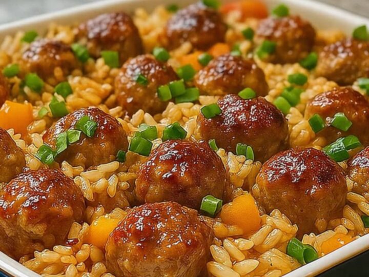 A blue casserole dish filled with golden rice and glossy honey garlic meatballs, topped with fresh green onions.