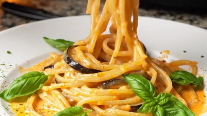 Creamy roasted eggplant spaghetti twirled on a plate, garnished with fresh basil leaves.