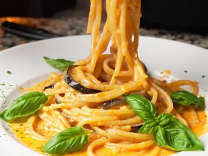 Creamy roasted eggplant spaghetti twirled on a plate, garnished with fresh basil leaves.