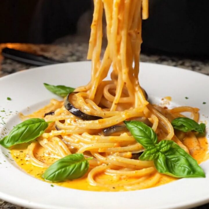 Creamy roasted eggplant spaghetti twirled on a plate, garnished with fresh basil leaves.
