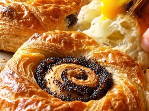 Golden spiral Turkish açma pastries with poppy seed filling on a parchment-lined baking sheet
