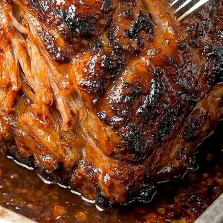 A close-up of a perfectly slow-roasted pork shoulder with a glistening honey garlic glaze in a metal pan.