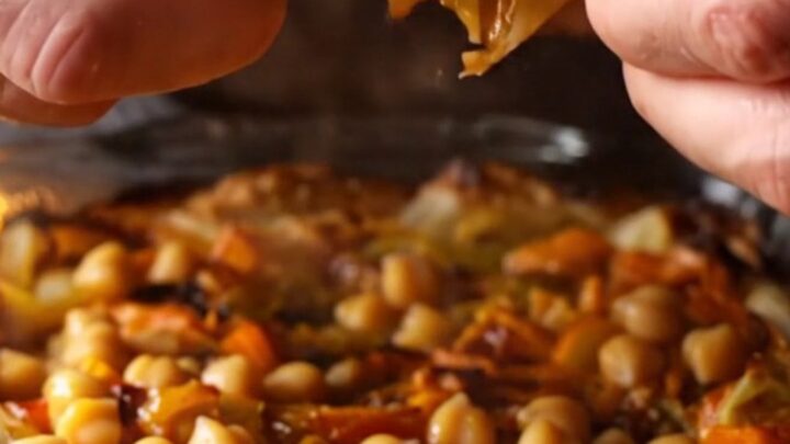Baked chickpea tava in a glass dish with caramelized peppers and tomatoes, served with flatbread
