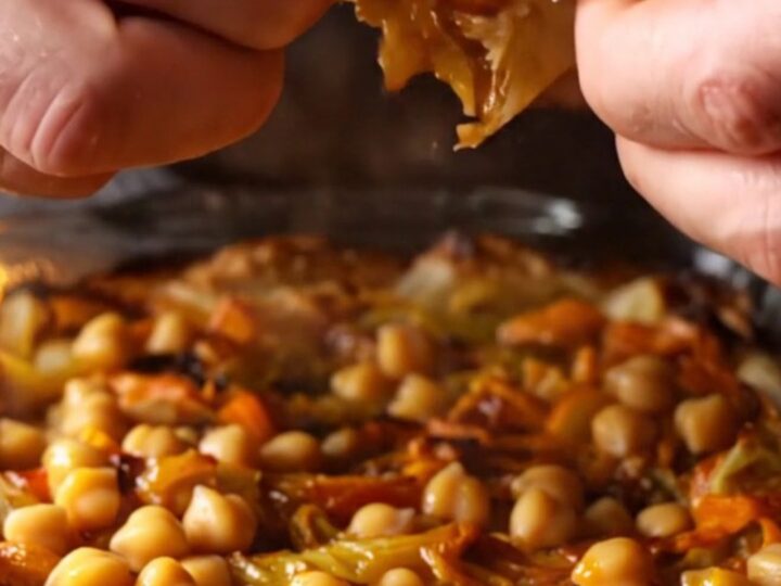Baked chickpea tava in a glass dish with caramelized peppers and tomatoes, served with flatbread