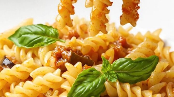 A fork twirls fusilli coated in a rich tomato and eggplant ragù with basil leaves