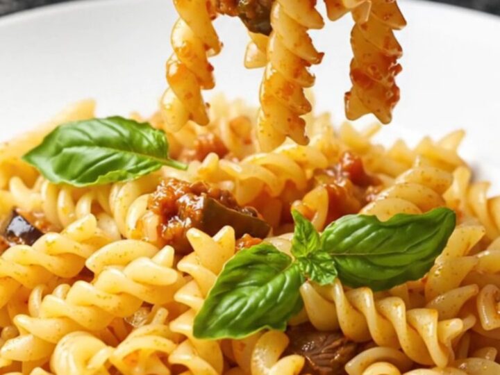 A fork twirls fusilli coated in a rich tomato and eggplant ragù with basil leaves