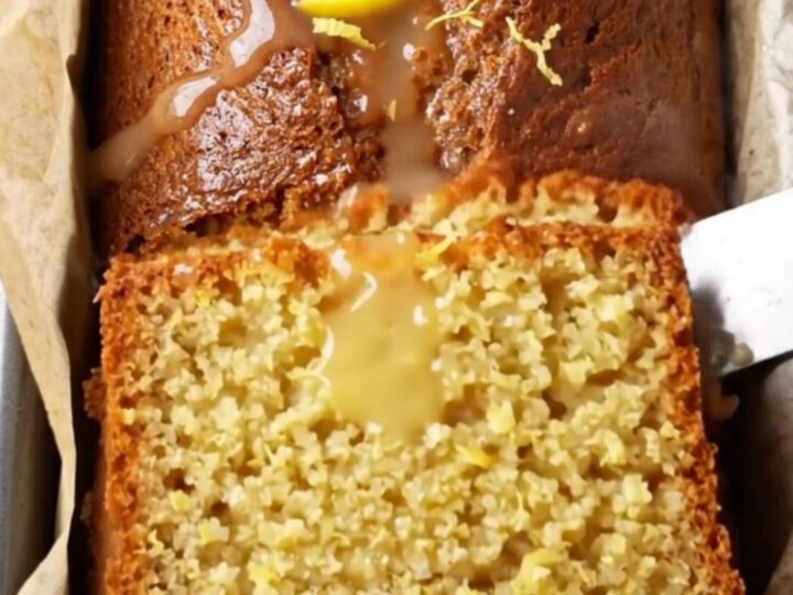 Moist whole-lemon cake with glossy white glaze and lemon zest on a cooling rack
