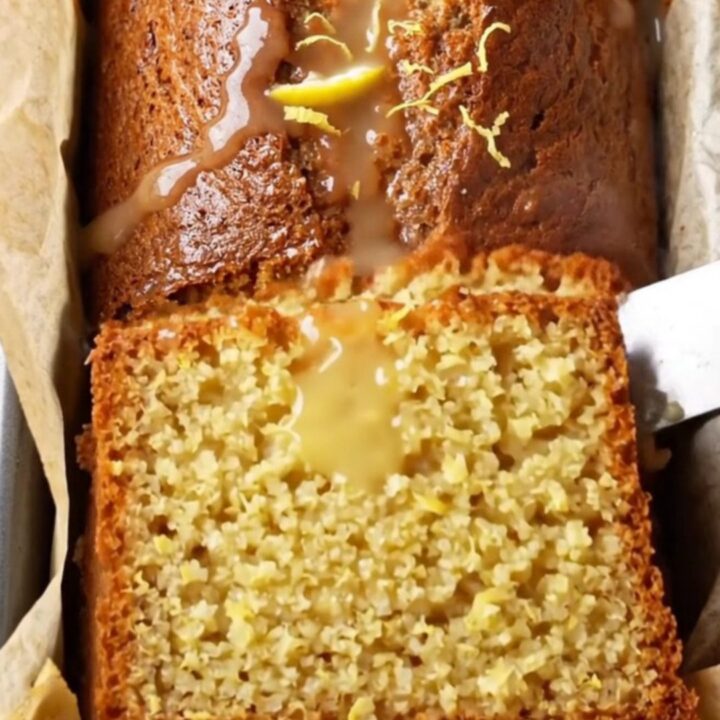 Moist whole-lemon cake with glossy white glaze and lemon zest on a cooling rack