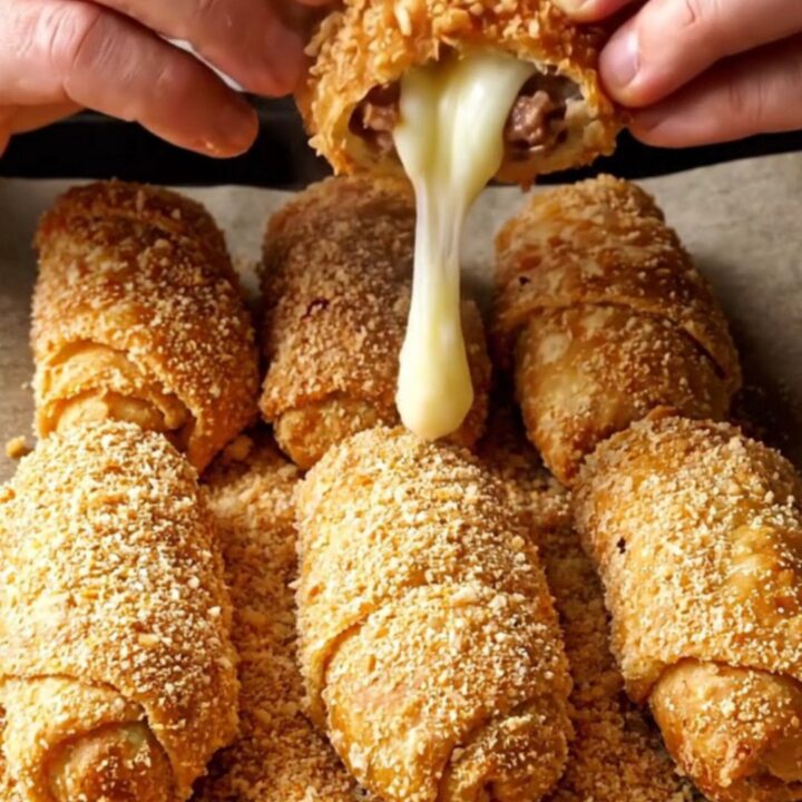 Golden crispy breaded meat börek rolls on a baking sheet, one snapped in half showing melted cheese.