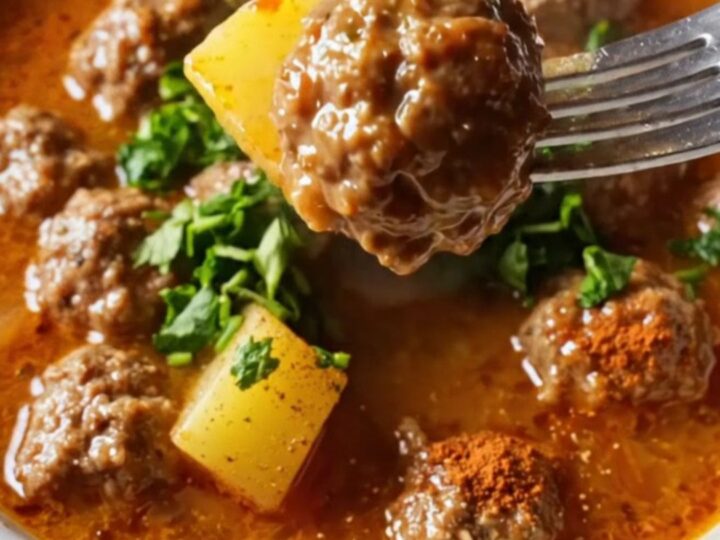 Golden meatballs and tender potatoes in a rich red sauce, garnished with fresh parsley, in a shallow bowl.
