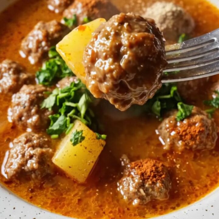 Golden meatballs and tender potatoes in a rich red sauce, garnished with fresh parsley, in a shallow bowl.