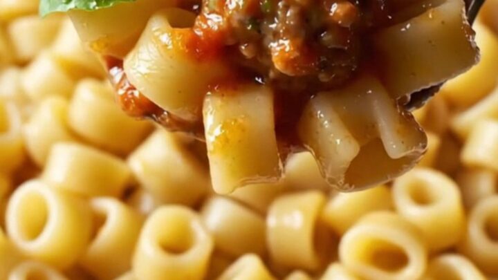 A skillet filled with glossy ditalini pasta and mini meatballs in tomato sauce, garnished with fresh basil.