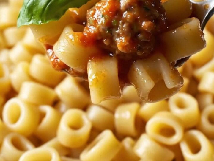 A skillet filled with glossy ditalini pasta and mini meatballs in tomato sauce, garnished with fresh basil.