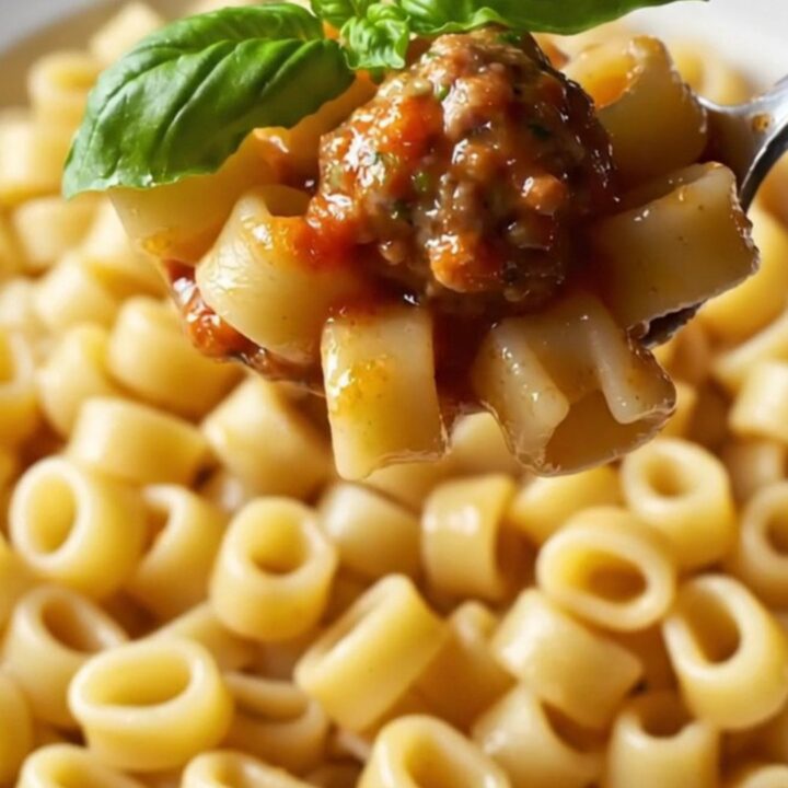 A skillet filled with glossy ditalini pasta and mini meatballs in tomato sauce, garnished with fresh basil.