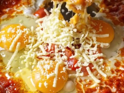 Menemen skillet with melted cheese and runny egg yolks, garnished with fresh herbs