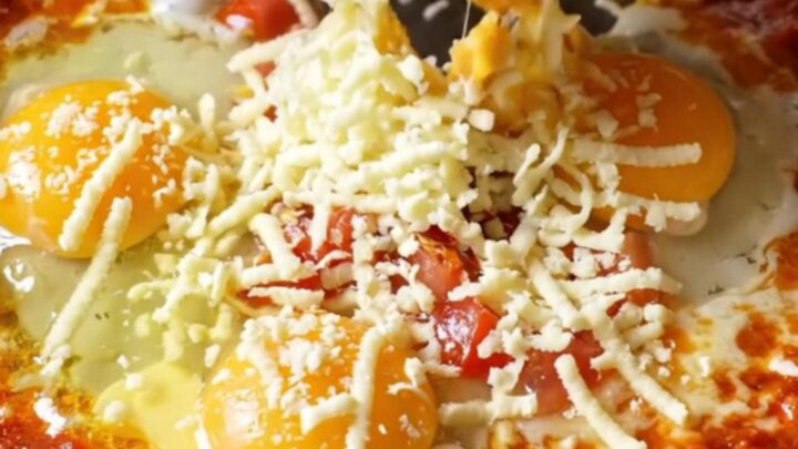 Menemen skillet with melted cheese and runny egg yolks, garnished with fresh herbs