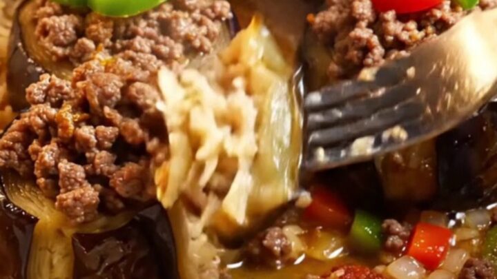 Golden stuffed eggplant cups with spiced beef, topped with tomato and pepper, in a baking dish with tomato broth.