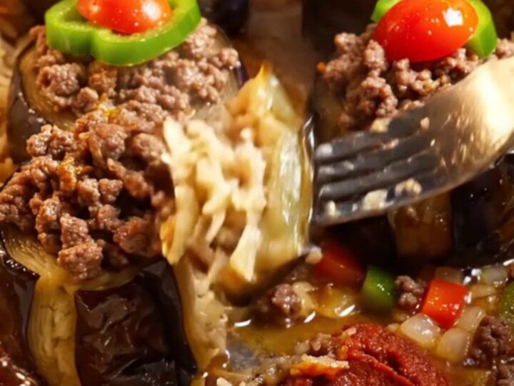 Golden stuffed eggplant cups with spiced beef, topped with tomato and pepper, in a baking dish with tomato broth.