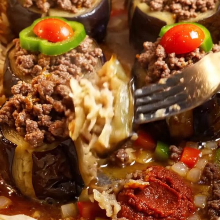 Golden stuffed eggplant cups with spiced beef, topped with tomato and pepper, in a baking dish with tomato broth.