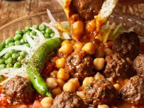 Baked Turkish tava with meatballs, chickpeas, and peas in a rich tomato sauce, with a piece of pita dipped in the center.