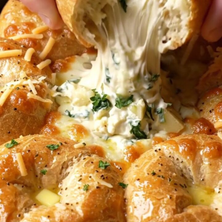 Cast iron skillet with golden bagel chunks around a bubbling spinach artichoke dip, with melted cheese stretching