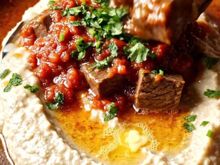 Spoon scooping braised beef over smoky eggplant puree on a ceramic plate