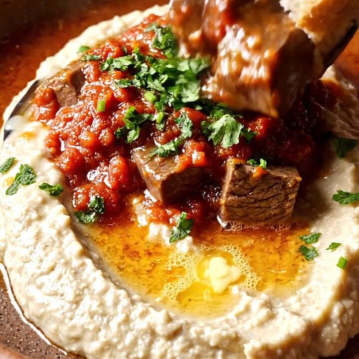 Spoon scooping braised beef over smoky eggplant puree on a ceramic plate