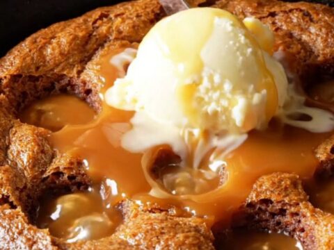 Warm sticky toffee date pudding in a cast-iron skillet, drenched in caramel sauce with a scoop of melting vanilla ice cream.