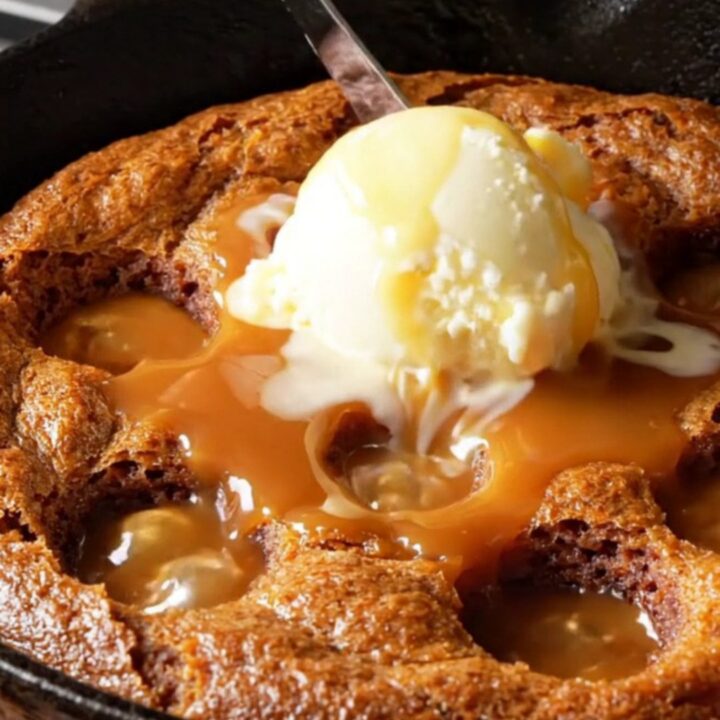 Warm sticky toffee date pudding in a cast-iron skillet, drenched in caramel sauce with a scoop of melting vanilla ice cream.