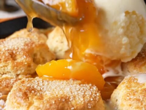Cast iron skillet filled with bubbling peach cobbler topped with golden biscuits