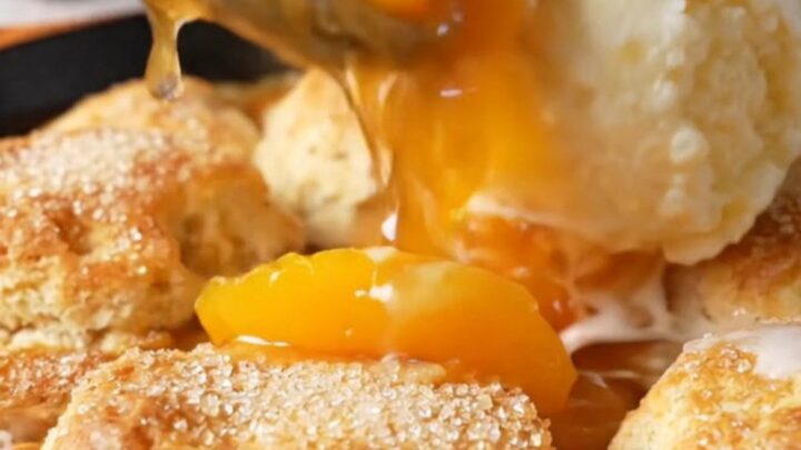 Cast iron skillet filled with bubbling peach cobbler topped with golden biscuits